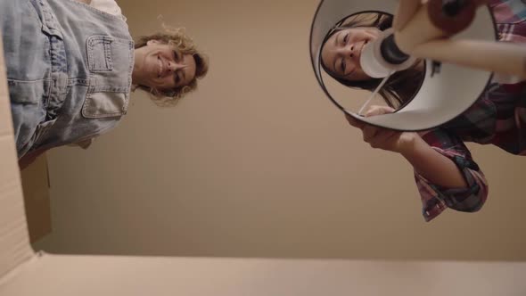 View From Inside a Cardboard Box of Two Cheerful Young Caucasian Girls Packing Household Things