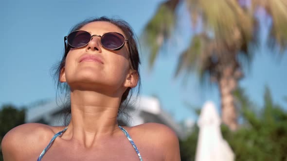 Closeup Tanned Face of Smiling Brunette Woman in Sunglasses Enjoying Sunbathing in Bikini on Beach