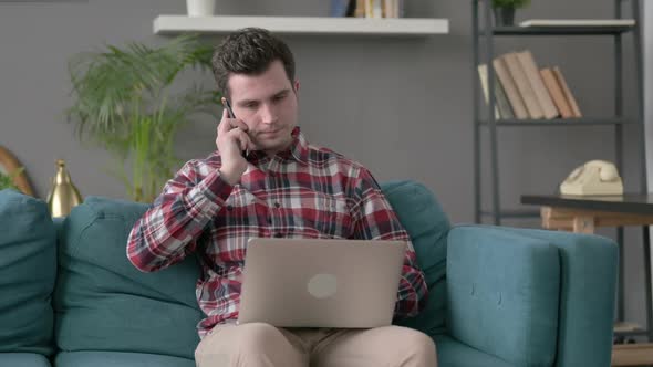 Man with Laptop Talking on Smartphone on Sofa