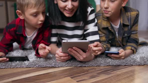 Mother and Two Sons which Resting on the Floor at Home and Watching Interesting Video