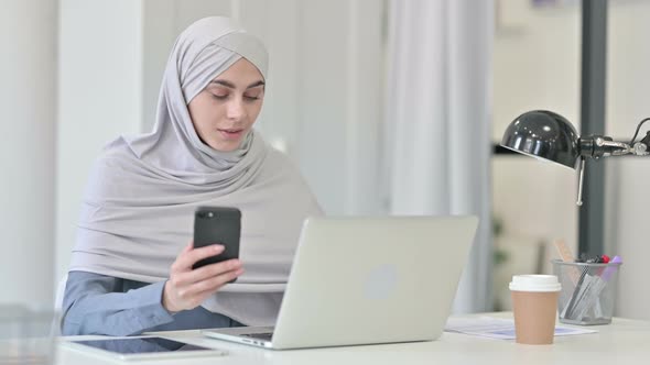 Young Arab Woman with Laptop Using Smartphone in Office