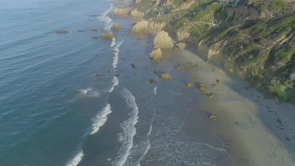 Aerial shots of El Matador beach over breaking waves and rocks on a hazy summer morning in Malibu, C