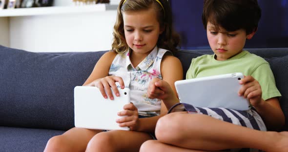 Siblings using digital tablet in living room