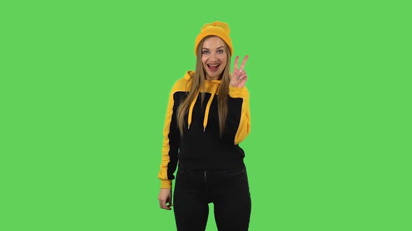 Modern Girl in Yellow Hat Is Showing Two Fingers Victory Gesture. Green Screen