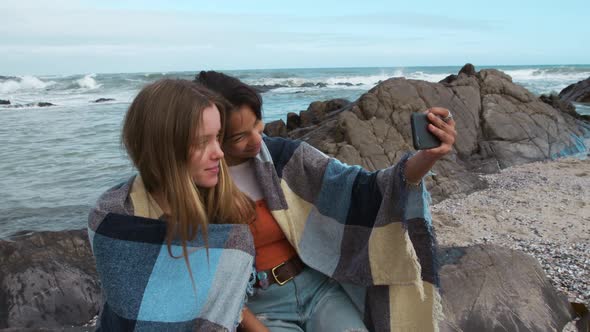 Side view of a Caucasian and a mixed race girl taking selfie seaside