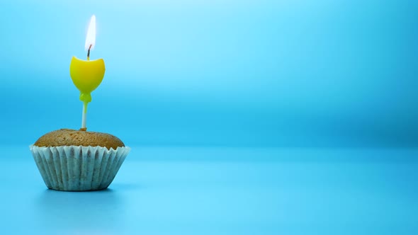 Baking Cupcake With A Burning Festive Candle On A Blue Background.