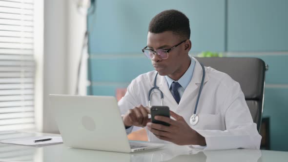 Young African Doctor Using Smartphone While Using Laptop in Office