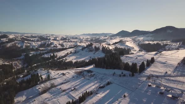 Aerial view of small village with scattered houses on snow covered hills in winter