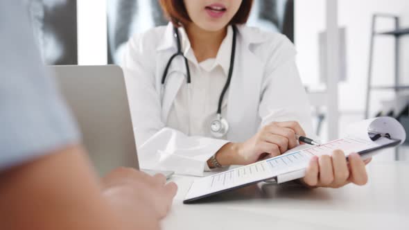 Young Asia female doctor using clipboard is delivering great news talk with male patient.