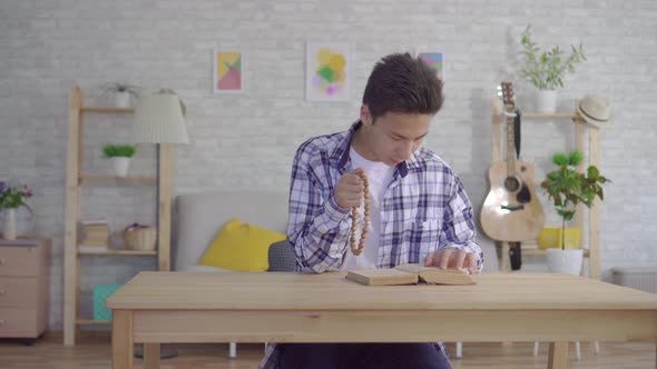 Young Asian Man with a Rosary in His Hand Reading a Bible alt