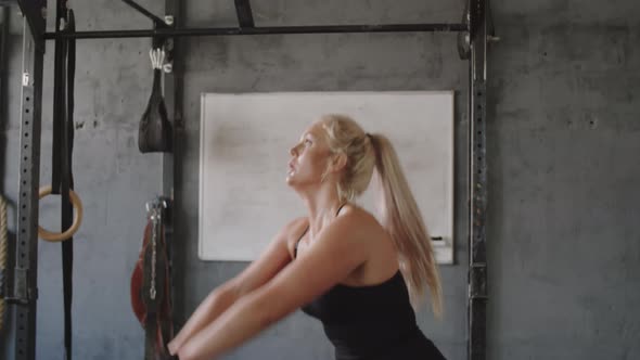 Sportswoman Doing Kettlebell Squats with Front Raises in Gym alt