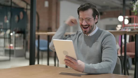 Young Man Celebrating Success on Tablet in Office