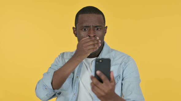 Young African Man Loss on Smartphone, Yellow Background 