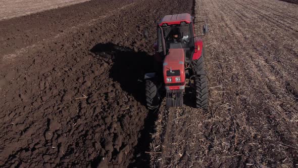 red tractor with a driver in the cab plows a field in Ukraine