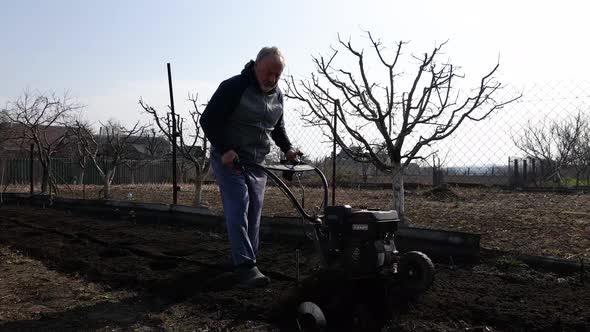 Man Farmer Working in the Garden Plows with Garden Tiller