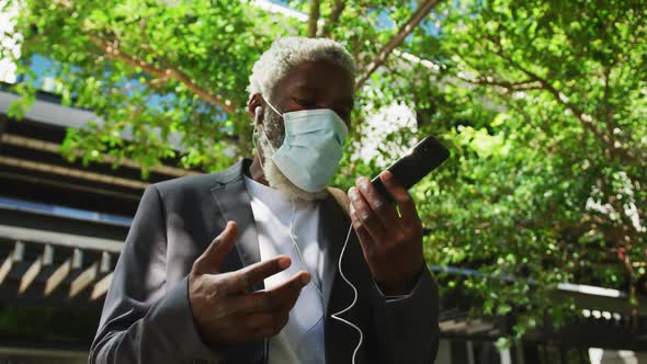 African american senior man wearing face mask talking on smartphone in corporate park