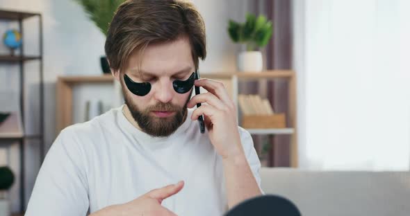 Young Bearder Which Touching Black Collagen Patches Under Eyes while Talking on Mobile
