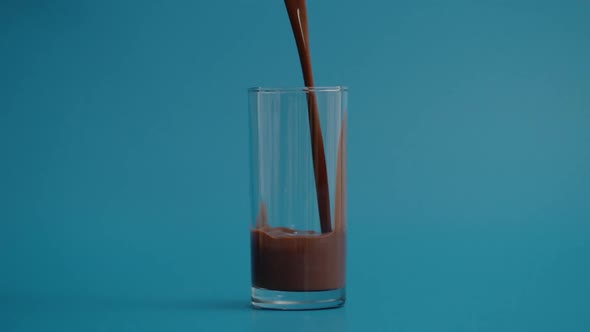 Super Slow Motion of Pouring Chocolate Milk in Transparent Glass Blue Background