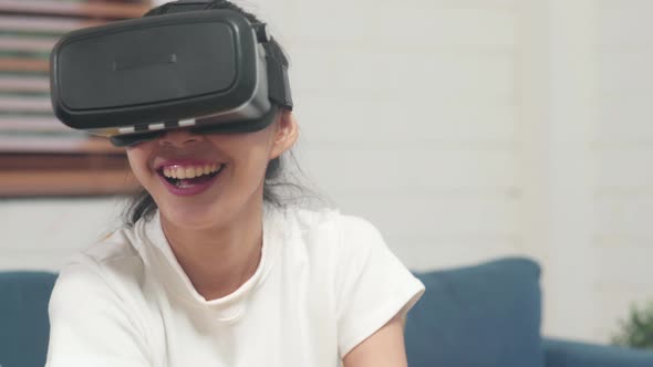 Asian teenager woman using glasses virtual reality simulator playing video games in living room.