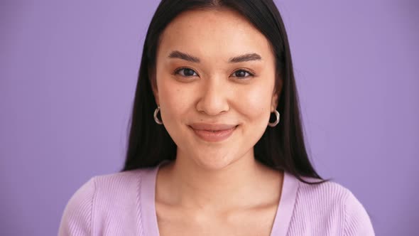 Happy Asian brunette woman wearing purple t-shirt looking at the camera