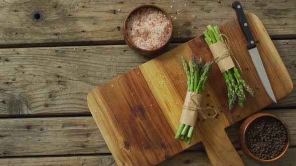 Video of two fresh asparagus bundles on wooden chopping board with knife and salt and pepper