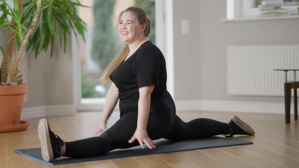 Wide Shot of Happy Plump Young Woman Rejoicing Success Sitting in Twine Pose on Exercise Mat