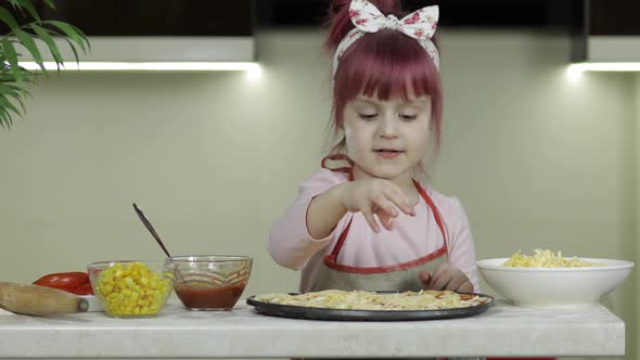 Cooking Pizza. Little Child in Apron Adding Grated Cheese To Dough in Kitchen