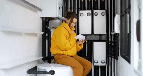 Confused Woman with Household Bills in the Boiler Room