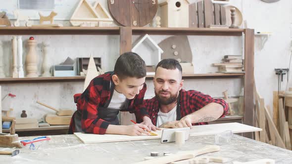 Dad Is Helping His Son To Mark Up Lines on Wooden Plank with Ruler