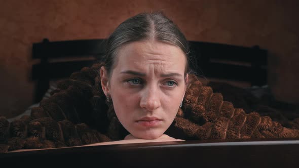 Young Girl is Sad Lying on a Bed Under a Blanket Closeup