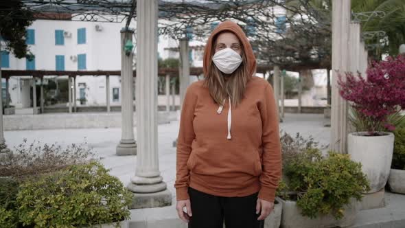 Woman in orange sweater and medical mask stay on empty street. Coronavirus pandemic concept.