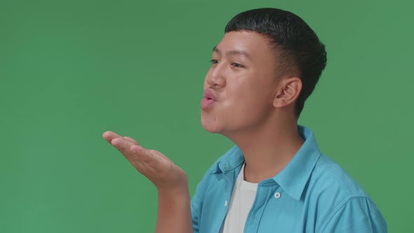 Side View Of Young Asian Boy Blowing Kisses To A Camera In The Green Screen Studio