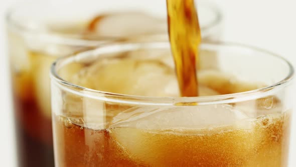 Pouring Cola Soft Drink with Ice Cubes Into a Glass