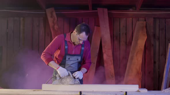 Carpenter Cleans Surface of Wooden Beam with Electric Planer and Flies Sawdust