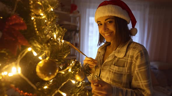 Slow Motion Portrait p of Happy Woman in Santa Hat Hangs Up Golden Ball on Branch of Christmas Tree