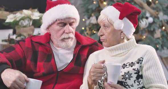 Close-up Portrait of Upset Mature Caucasian Man and Woman Sitting with Coffee at the Background