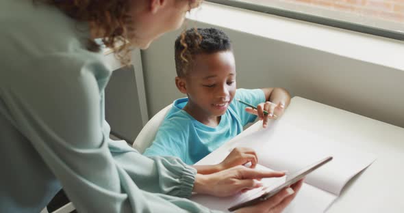 Video of happy caucasian female teacher explaining lesson on tablet to african american boy