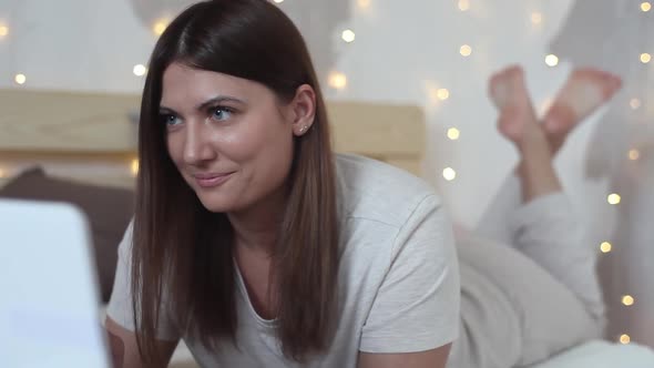 Beautiful Girl Enjoys a Laptop Lying on the Bed