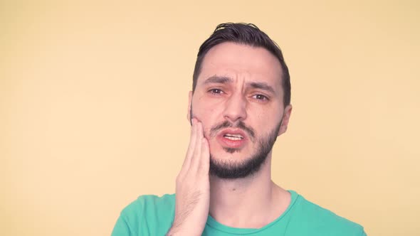 Young Man with Helpless Face in Pain From Toothache Holding Hand Against His Cheek