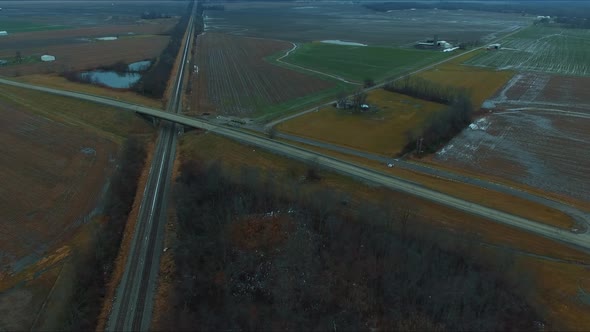 Cars, trucks and a bus traveling across an overpass running over railroad tracks next to a pond on a