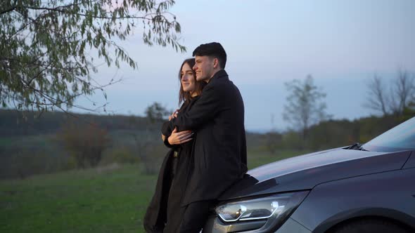 Happy Loving Couple of Travelers Stand Next to Car and Admire Beautiful Sunset