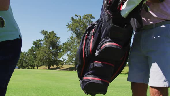 Caucasian senior couple walking with their golf bags at golf course on a bright sunny day