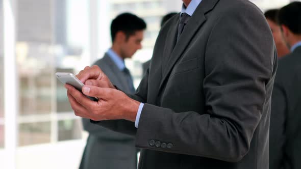 Businessman using smartphone with his colleagues behind him