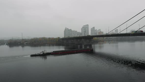 Small tugboat with sand scow sailing on wide calm river in industrial city with smog and fog