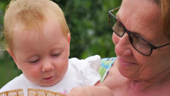 Smiling infant on grandmothers hands. Granddaughter with grandmother on sunny summer day