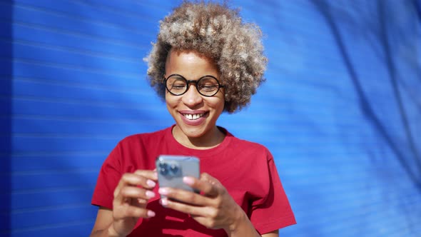 Positive African woman wearing red t-shirt texting by phone