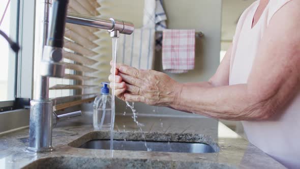 Mid section of senior caucasian woman washing her hands in the sink at home