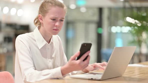 Disappointed Young Businesswoman Using Smartphone and Laptop 