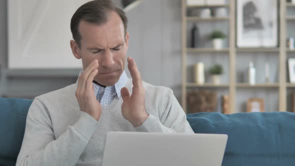 Middle Aged Man with Headache Working on Laptop While Sitting on Couch