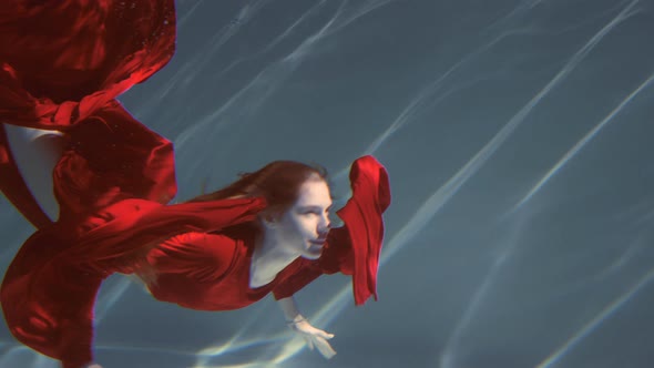 Attractive Redhaired Young Woman Swims Beautifully Underwater in a Red Dress